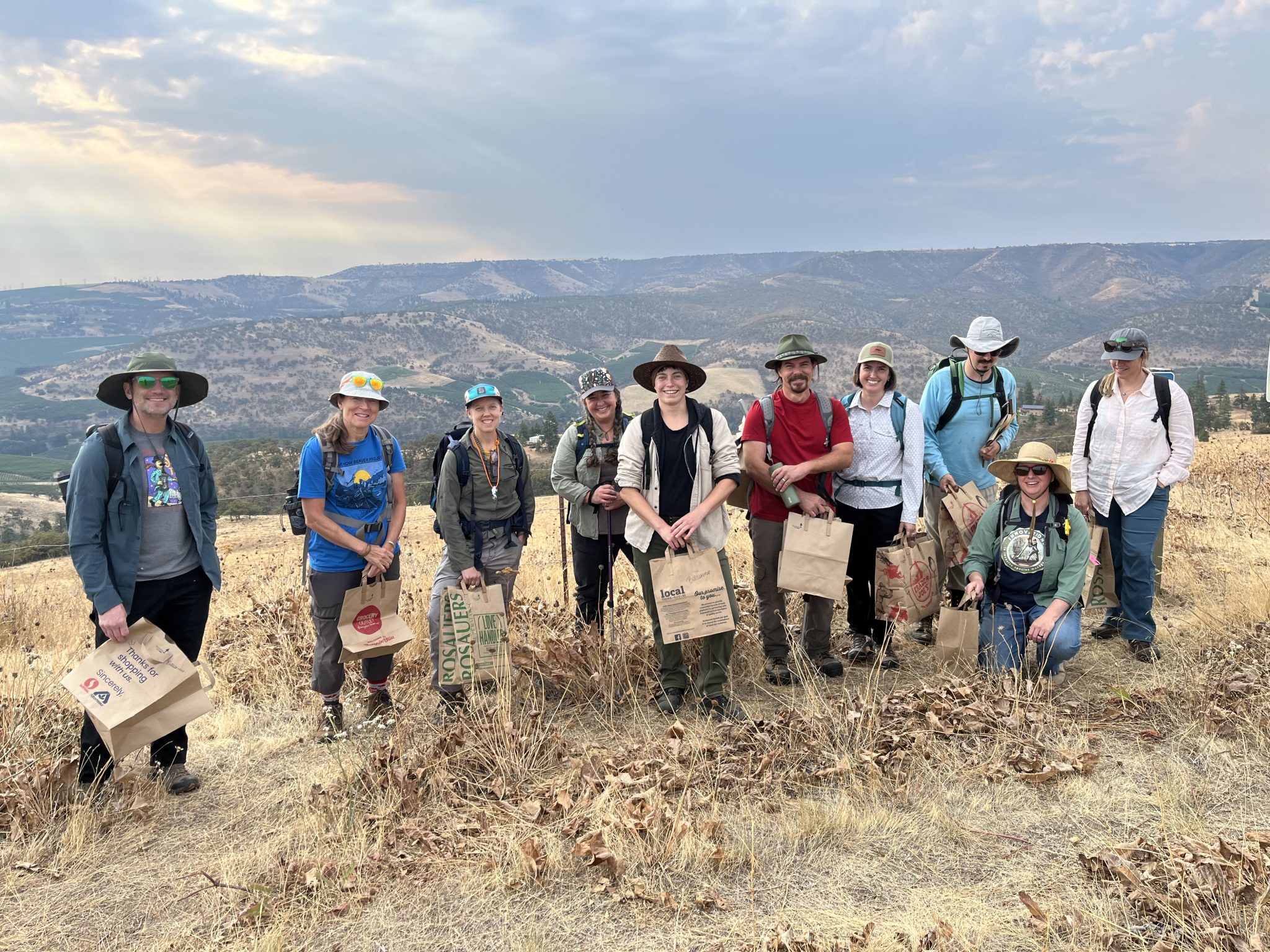 A group of people stands in a field holding bags of seeds they have collected.