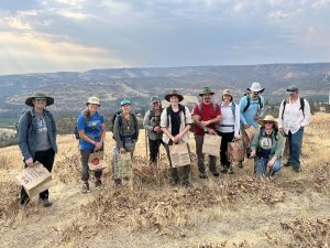 A group of people stands in a field holding bags of seeds they have collected.