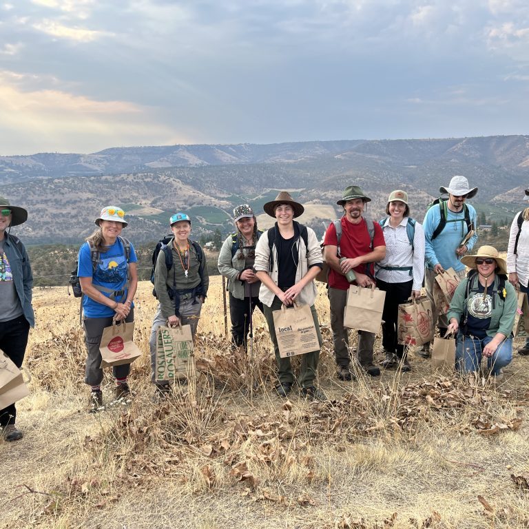 A group of people stands in a field holding bags of seeds they have collected.
